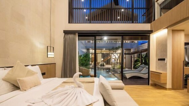A modern hotel room with a bed, a sofa, a glass door leading to a pool area, and a view of the outdoors. - X Samata (Bali)