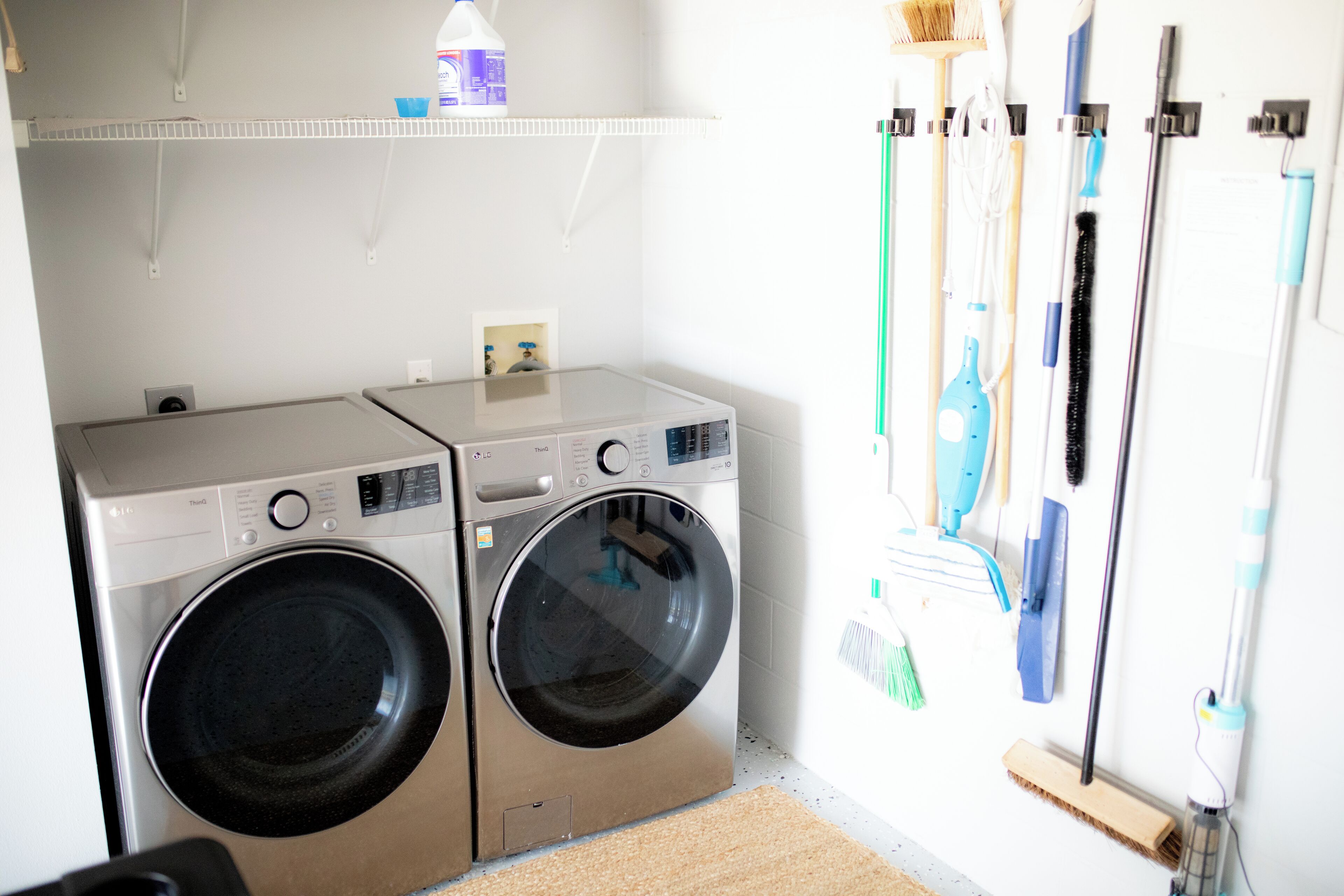 A laundry area with two front-loading washing machines and a drying rack with various cleaning tools.