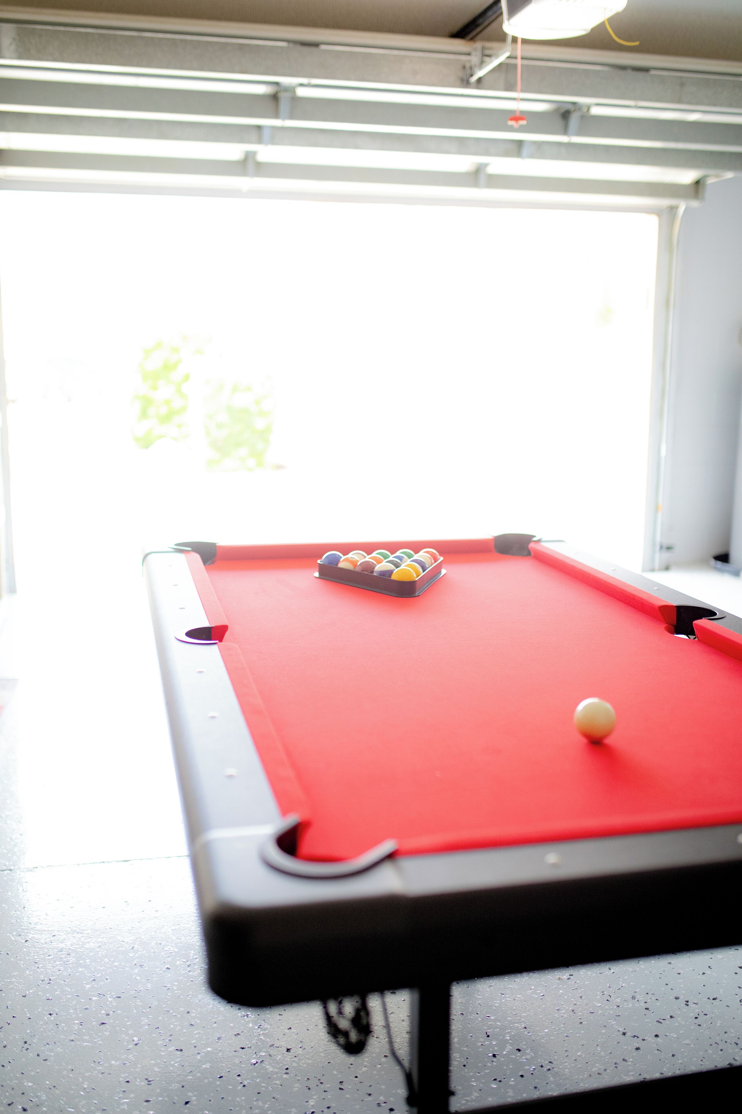 Ein Billardtisch mit Kugeln und Spielstange in einem Raum mit Fenster und Jalousien.