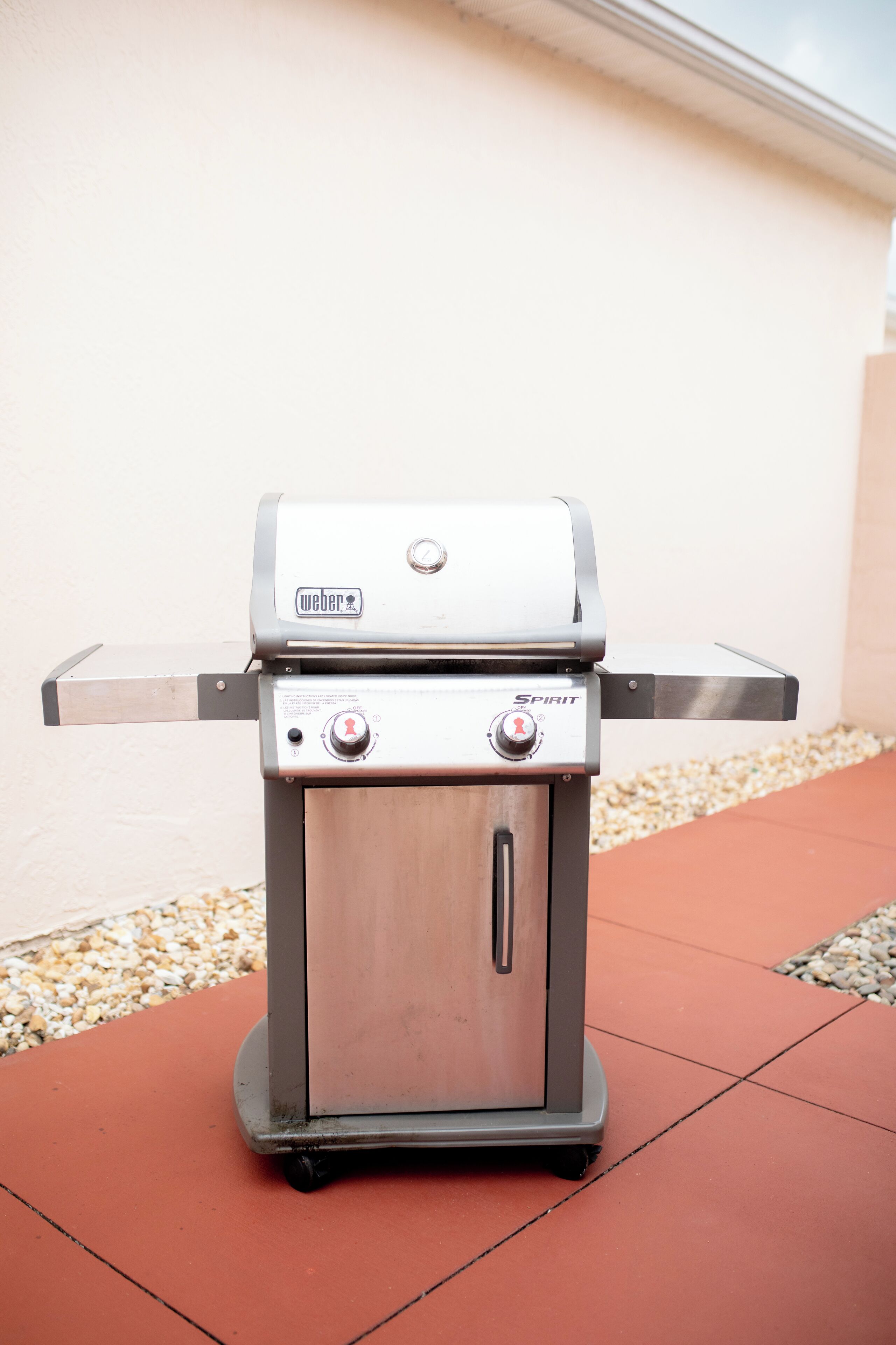 Un barbecue Weber Spirit portable, doté de deux boutons de contrôle et d’une étagère latérale, placé sur une terrasse carrelée.