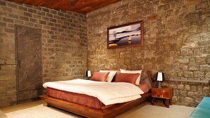 Ein Schlafzimmer mit einer Steinwand, einem Bett mit Holzrahmen, einem Nachttisch und einem Gemälde über dem Bett.