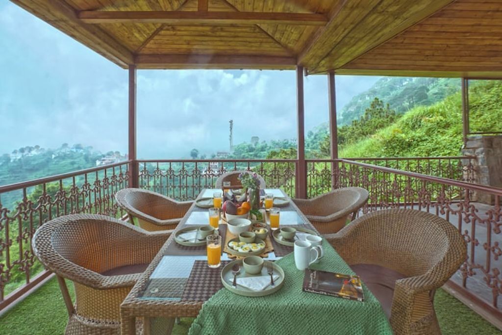 A dining area with wicker chairs and a table set for breakfast, overlooking a lush landscape.
