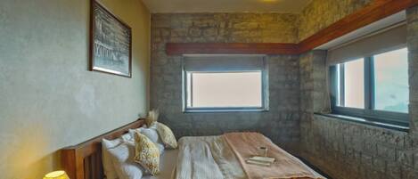 A bedroom with a stone wall, a bed with pillows, a window, and a ceiling fan.