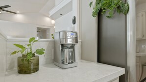 Une cuisine équipée d’une machine à café, d’un réfrigérateur et d’une plante en pot posée sur le plan de travail.