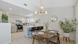 Une cuisine moderne avec des meubles blancs, un îlot central et un coin repas comprenant une table et des chaises en bois.