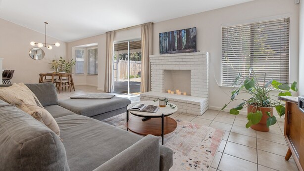 Un salon moderne avec un canapé gris, une table basse ronde, une cheminée et une grande fenêtre équipée de stores.