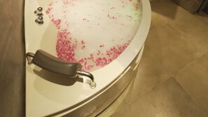A bathtub with pink flower petals in the water, a faucet, and a showerhead. - 3 Bhk Penthouse|Jacuzzi | Pool Table|The Opulence (panchkula)