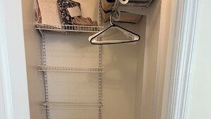 Un vestidor amplio con varias estanterías y una barra para colgar ropa, suelo de madera y paredes blancas.