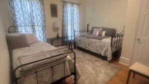 Un dormitorio con dos camas, una mesita de noche, una lámpara y una silla.