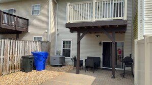 Ein überdachter Patio-Bereich mit Außenmöbeln, einem Grill und einer Mülltonne.