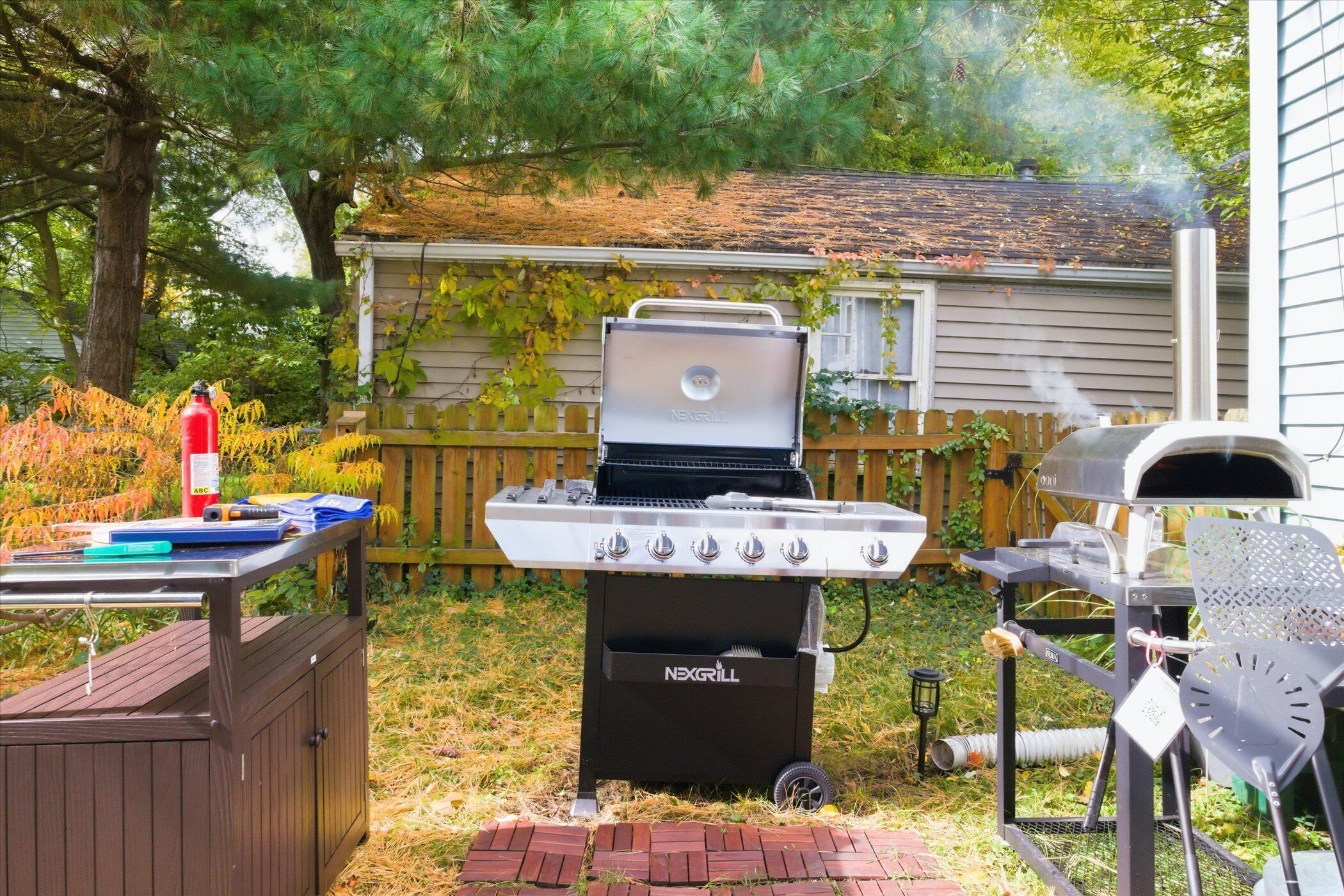 A backyard with a grill, a pizza oven, and a fire extinguisher.