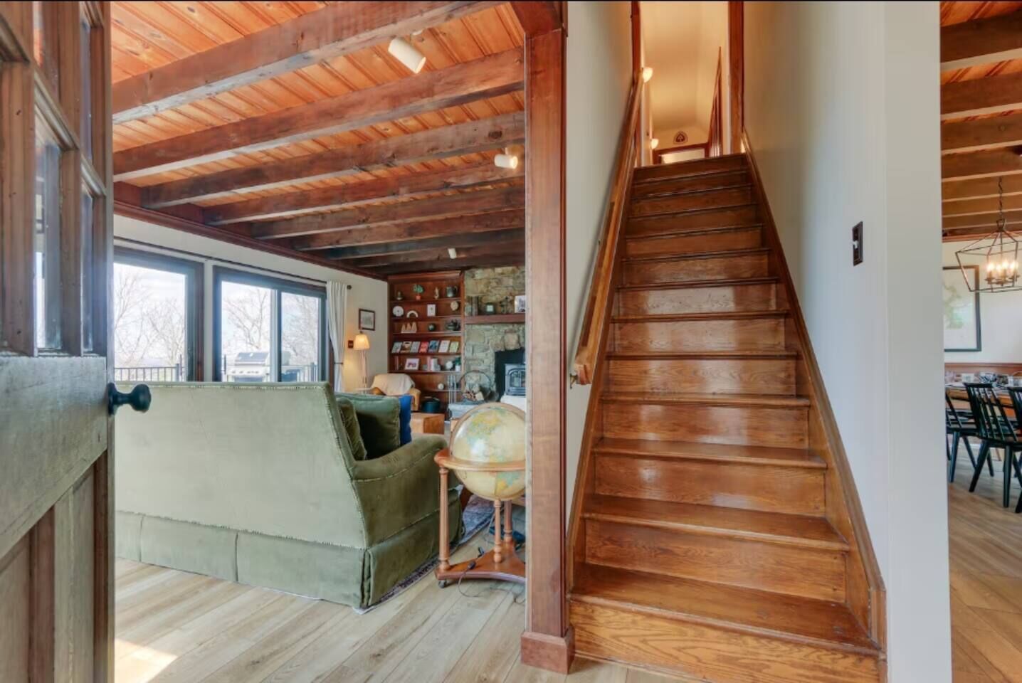 A wooden staircase leading to a dining area with a view of a cozy living room and a fireplace.