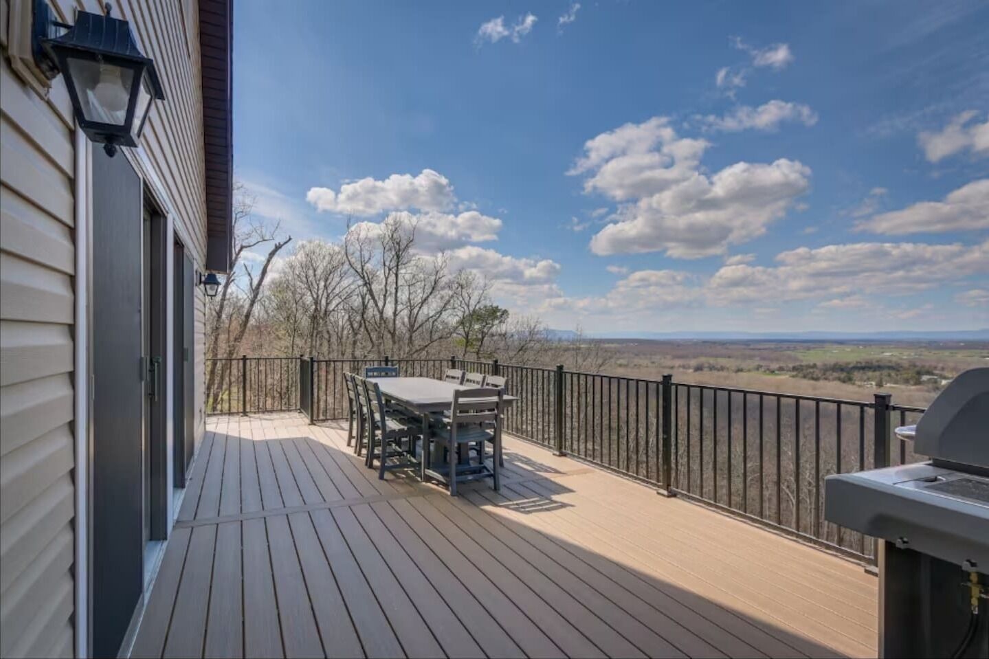 Eine Holzterrasse mit Tisch und Stühlen, einem Grill und Blick auf die Landschaft.