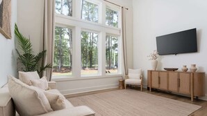 A living room with a large window, a flat-screen TV, a sofa, a chair, and a wooden cabinet.