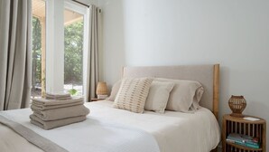 A neatly made bed with a stack of folded towels, a bedside lamp, and a small wooden side table with books.