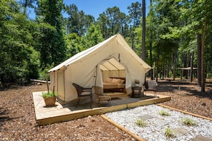 A tent with a bed, two chairs, a small table, and a potted plant.