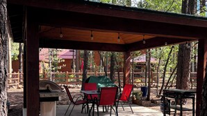 An outdoor patio with a covered seating area, a grill, and a dining table with chairs. - Charming 3-bedroom mountain house in the pines @ Pinetop Country Club (Pinetop Country Club)
