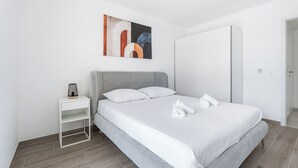 Un dormitorio moderno con una cama gris, mesitas de noche blancas y un gran armario.