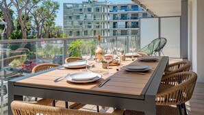 Un área de comedor en un balcón con una mesa de madera para cuatro, sillas de mimbre y vistas de la ciudad.