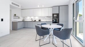 Una cocina moderna con armarios blancos, encimera de mármol y una mesa redonda con sillas grises.