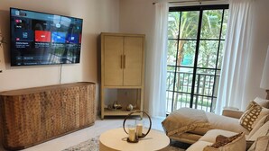 Ein modernes Wohnzimmer mit Flachbildfernseher, Deckenventilator, Holzschrank, rundem Couchtisch und einer Couch mit Kissen.