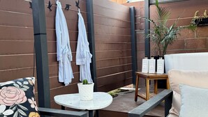 En terrasse med et rundt bord, polstrede siddepladser, en potteplante og et træhegn.