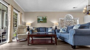 A living room with a sofa, armchair, and coffee table. There is a painting on the wall and a window with curtains. - Quiet 1st-Floor w/ Pool Views Near Myrtlewood Golf | MW 4665-104 (Myrtle Beach)