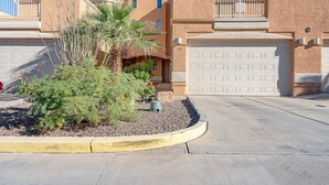 Un edificio residencial con garaje, un pequeño jardín con una palmera y un cielo azul despejado.