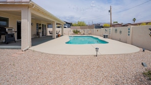 Un jardin avec une piscine, un patio couvert et un espace barbecue.