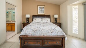 Une chambre à coucher avec un lit, deux tables de chevet avec des lampes, un tableau encadré au mur et une fenêtre avec des rideaux.
