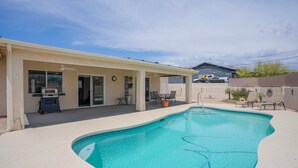 Une piscine avec un patio couvert, un barbecue et des espaces de détente en plein air.