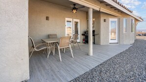 Eine überdachte Terrasse mit Tisch und Stühlen, einem Deckenventilator und einer Tür, die zu einer Garage führt.