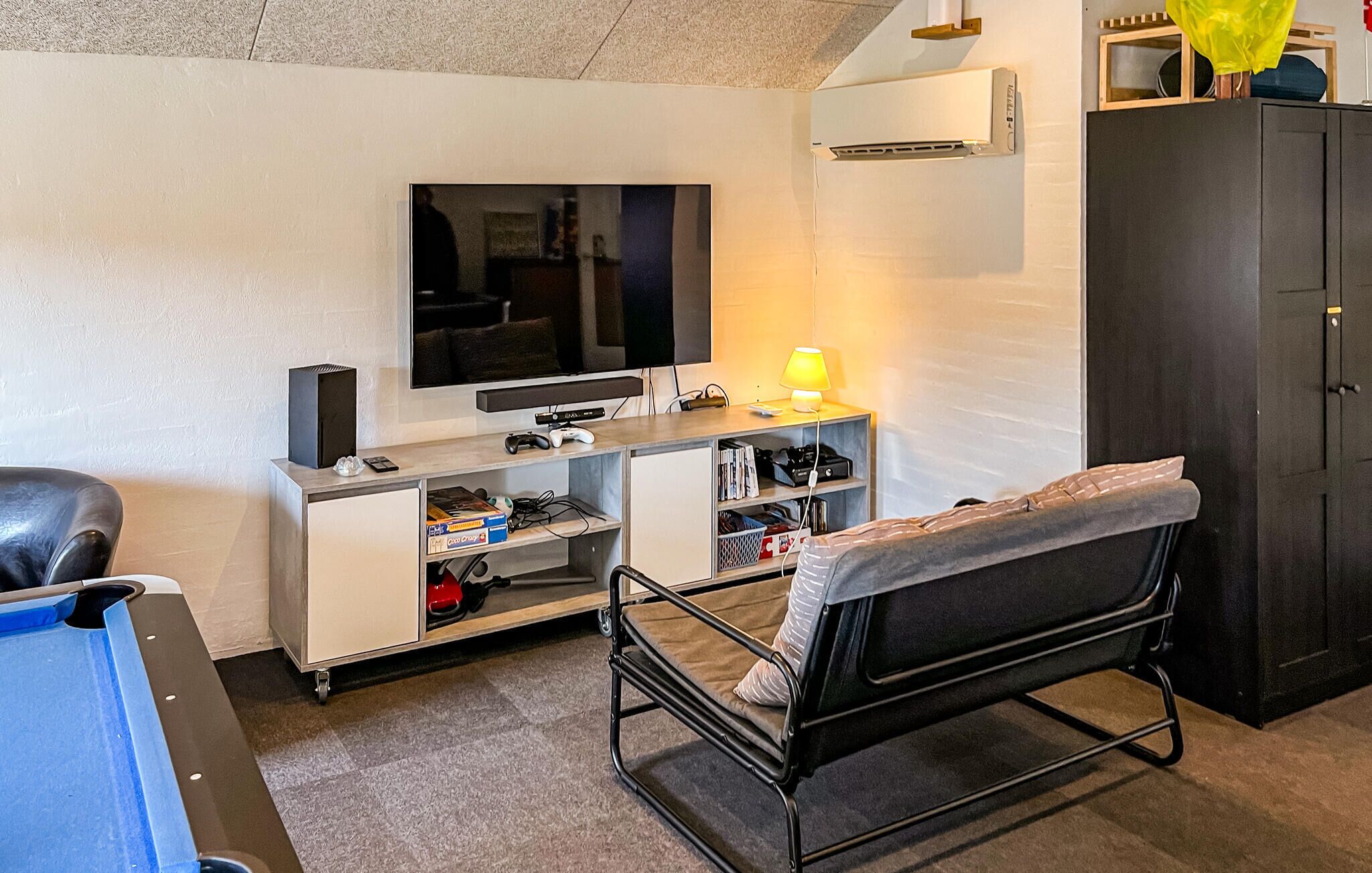 Een kamer met een televisie, een gameconsole en een bed met hoofdeinde.