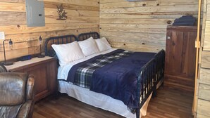 Un dormitorio con paneles de madera, una cama, una mesita de noche, una lámpara, un reloj y un equipo de aire acondicionado.