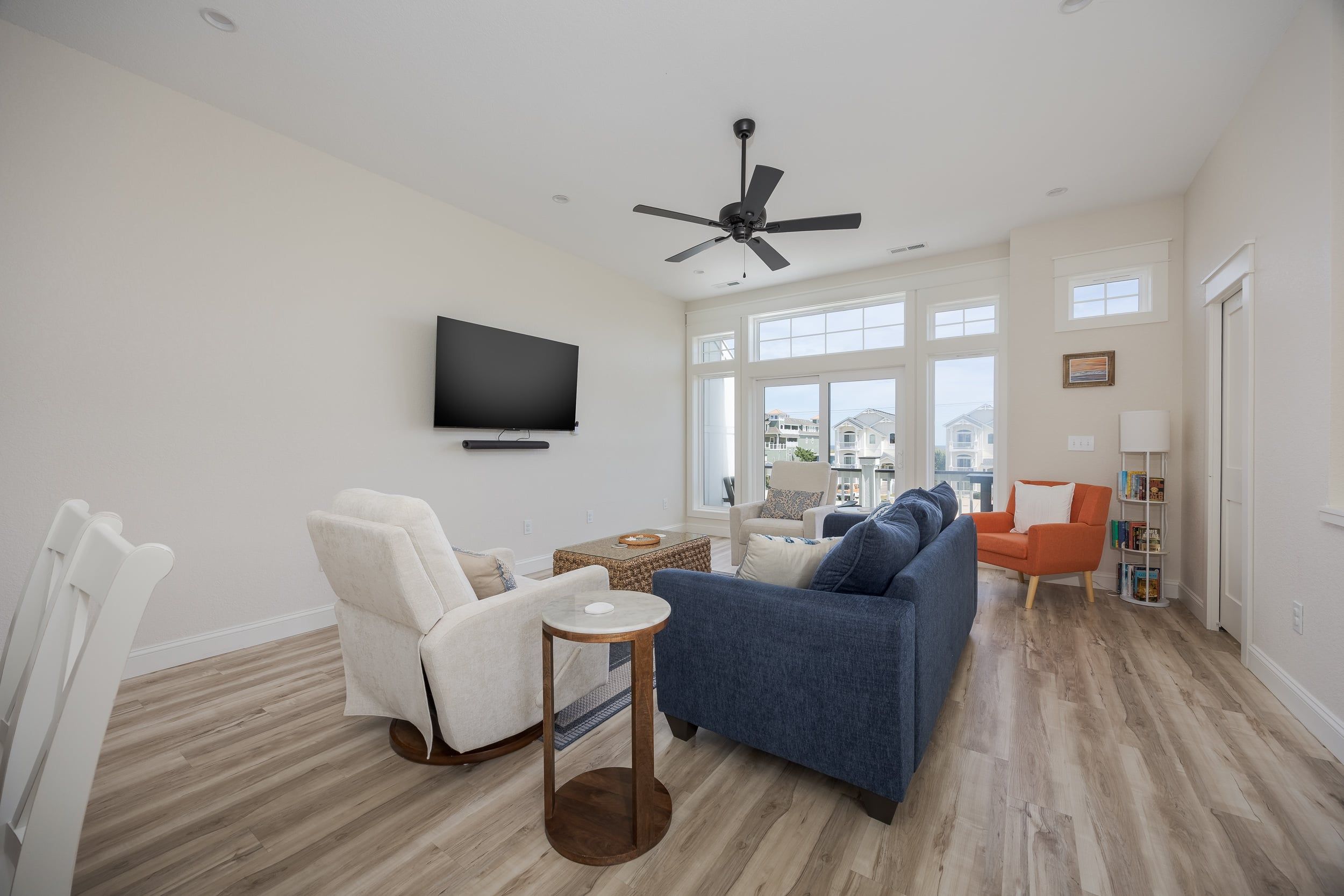 A modern living room with a flat-screen TV, a ceiling fan, and a large window offering a view of the outside.