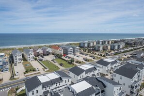 Un quartier résidentiel situé sur la côte, avec des immeubles à plusieurs étages, une plage en arrière-plan et un parking où sont garées plusieurs voitures.