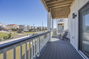 Una terraza de madera con barandilla blanca, una mesa y sillas, y vista a una calle residencial.