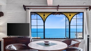 Una habitación con una mesa redonda, sillas, televisor y un ventanal con vistas al mar.