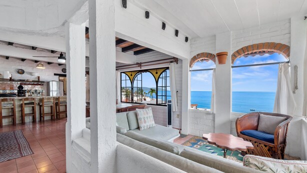 Una habitación amplia con balcón, zona de estar con sofá y sillones, y vista al mar.