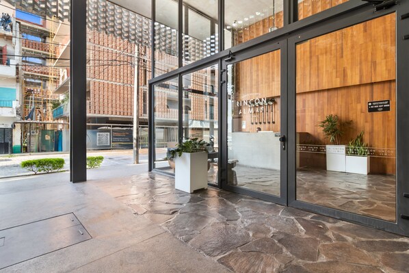 Una entrada de hotel moderna con suelo de piedra, grandes puertas de vidrio y paneles de madera.