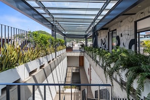 Un edificio moderno con un balcone in vetro, pareti in cemento e elementi verdi.