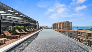 A rooftop pool with lounge chairs and a clear view of the ocean.