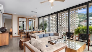 A modern living room with a glass coffee table, beige sofas, and a dining area with wooden furniture.