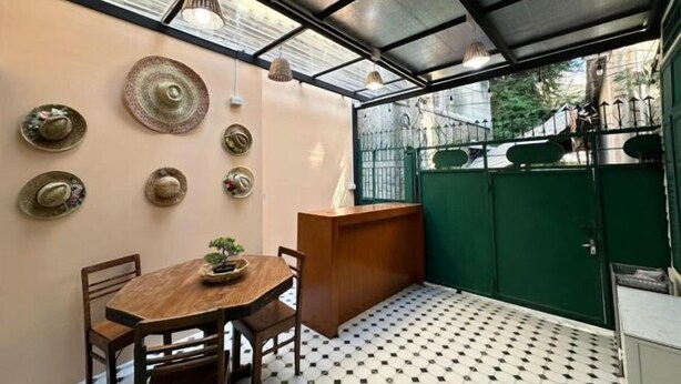A small, enclosed patio area with a round wooden table and chairs, a small plant on the table, and a green gate in the background. - Atlas Hostel Khaosan (Bangkok)