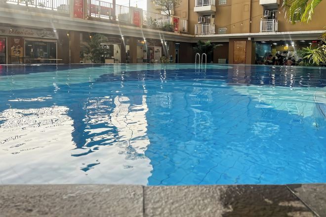 Ein Innenpool mit klarem Wasser, umgeben von einem Gebäude mit Balkonen und einem Restaurant namens "Ilian Cafe".