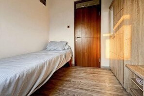 A small bedroom with a single bed, a wooden wardrobe, and a door leading to another room. - BEST View 2BR Apt Pluit w/ Pool WiFi & Netflix (North Jakarta)