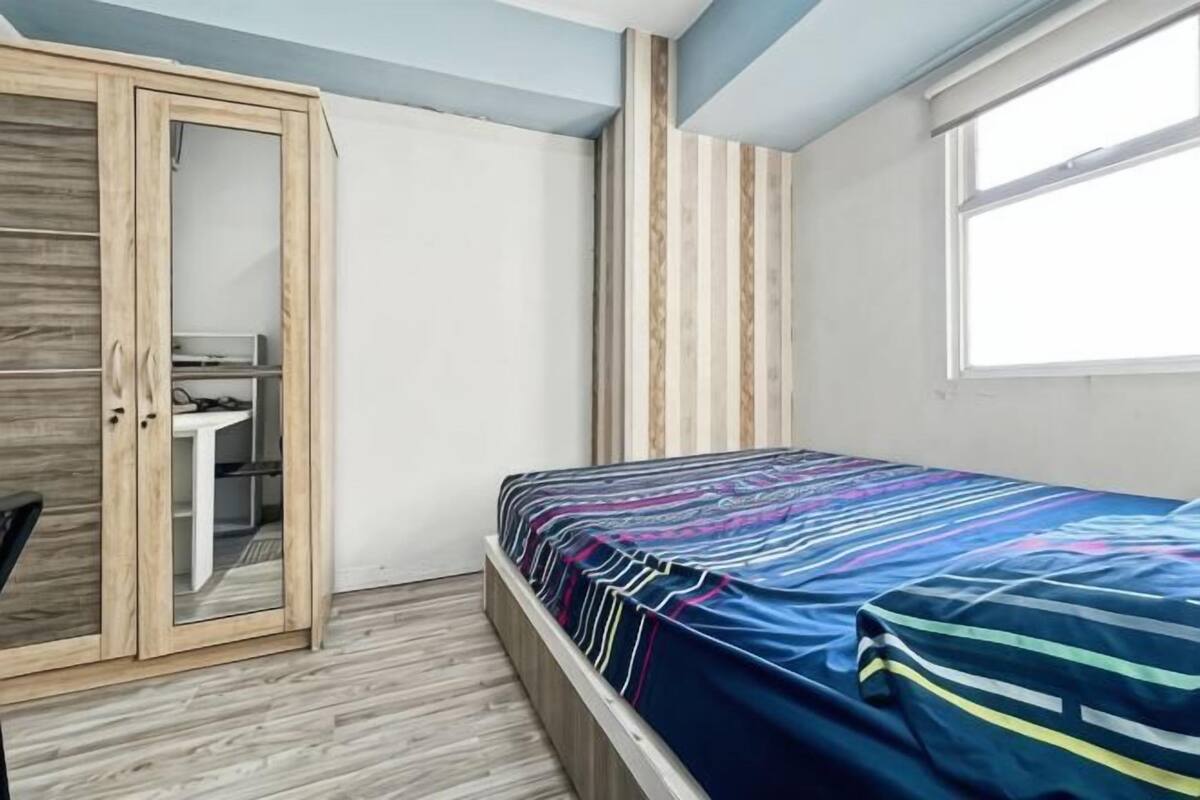 A bedroom with a bed, wardrobe, desk, and a window.