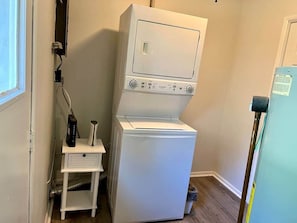 Un lavadero pequeño con lavadora y secadora apiladas, un armario blanco y un refrigerador azul.