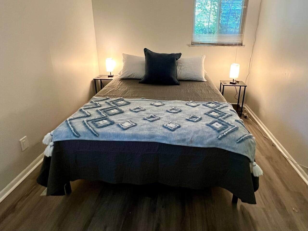 Une chambre à coucher avec un lit, deux tables de chevet et une fenêtre avec des stores.