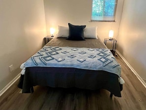 Un dormitorio con cama, dos mesitas de noche y una ventana con persianas.